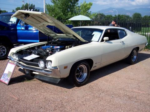 1972 Ford Ranchero - A cream 1970 Ford Torino GT coupe is displayed with its hood open, parked beside a blue pickup truck.