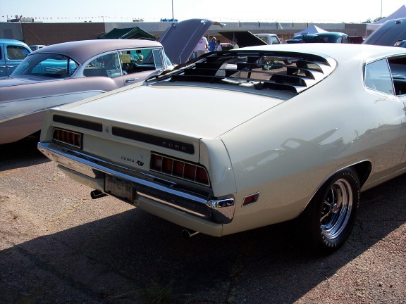 Rear of a cream-colored 1970 Ford Torino GT with louvers on the back window. Another car is parked to its left