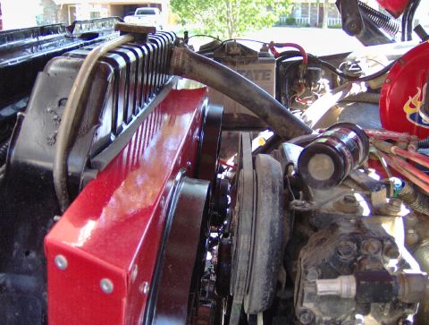 1978 Ford Bronco - Close-up of an open engine bay showing a red-painted radiator and shroud alongside a black cooling fan, V-belt pulleys and a curved upper r…
