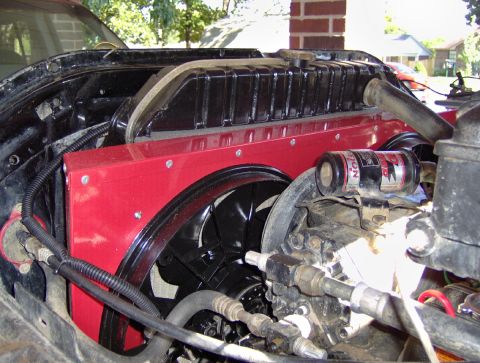 1978 Ford Bronco - Engine bay of a truck with the hood up, showing a black flex-blade fan behind a red-painted sheet-metal fan shroud and radiator top tank, w…