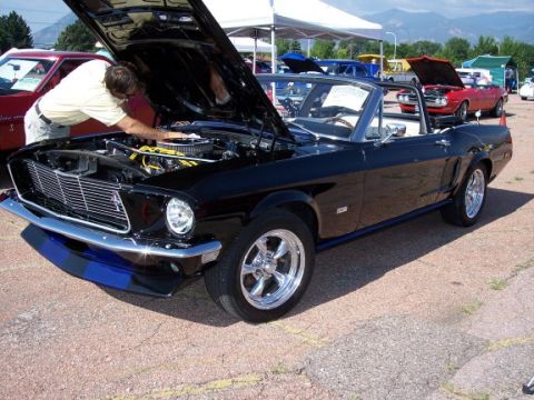 1972 Ford Ranchero - Man inspects engine of black 1969 Ford Mustang convertible at car show. Another car is visible.