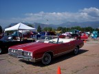 1972 Ford Ranchero - A red 1972 Oldsmobile Cutlass Supreme convertible is parked outdoors with other vehicles under a bright sky.