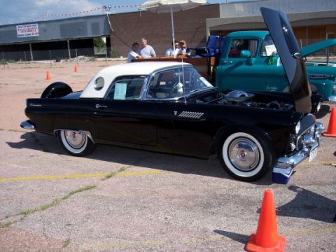 1972 Ford Ranchero - A black 1957 Ford Thunderbird with a white roof and continental kit is displayed at a show, with a teal truck in the background.