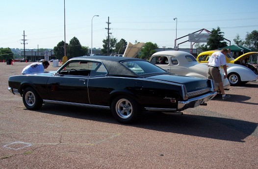 Black 1967 Mercury Cougar parked next to other cars. Someone is looking at the Cougar's engine