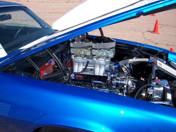 Blue car engine bay with dual carburetors, chrome components, and an open white hood