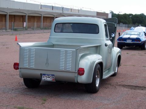 1972 Ford Ranchero - A light blue pickup truck is parked next to a blue Camaro, with an abandoned building in the background.