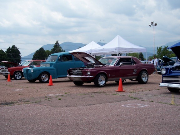 Maroon 1967 Ford Mustang coupe with hood open, parked at an outdoor car show