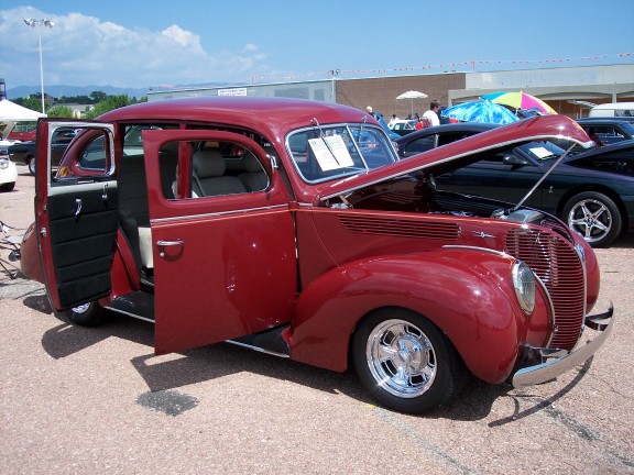 Red 1939 Ford sedan with hood and doors open, parked outdoors. Another car is visible behind it