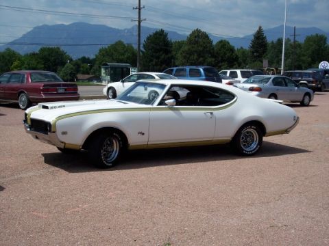 1972 Ford Ranchero - A white 1970 Oldsmobile 442 with gold racing stripes is parked in a lot with other vehicles.