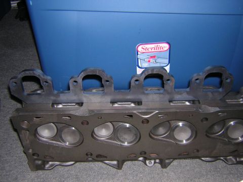 1979 Ford Bronco - Close-up of an engine cylinder head showing exhaust manifold flanges, with a Sterilite storage bin in the background.