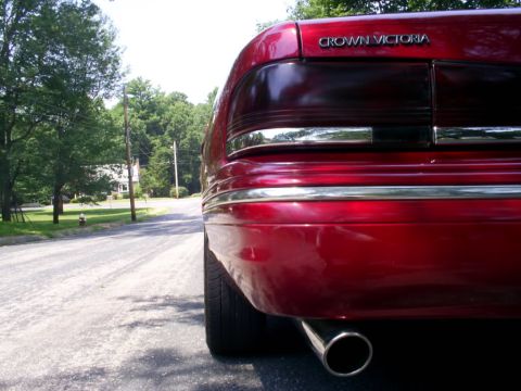 1995 Ford Crown Victoria - The rear of a red 1995 Ford Crown Victoria is visible with chrome accents and an exhaust pipe.