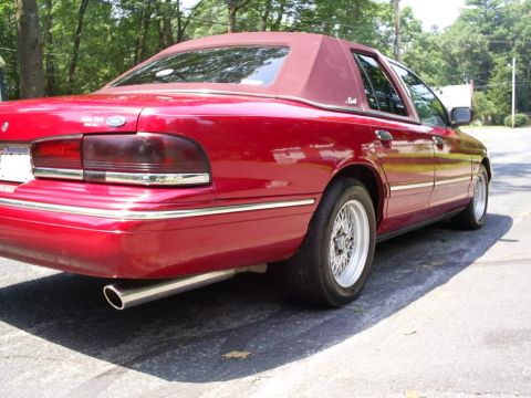 1995 Ford Crown Victoria - This red sedan features a vinyl top and a chrome strip along its side. The rear taillights are tinted.