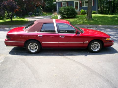 1995 Ford Crown Victoria - A red sedan with a vinyl roof is parked on a street in front of a house.