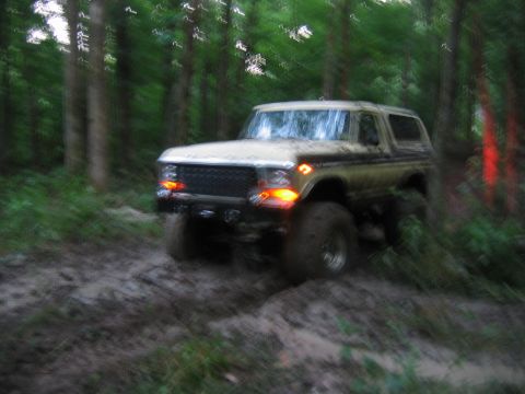 1992 Ford Mustang - Ford Bronco navigating a muddy trail in a forest setting.