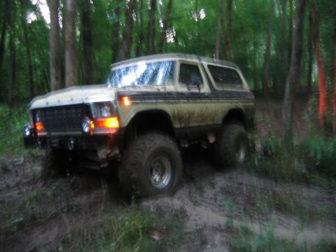 1992 Ford Mustang - This lifted Ford Bronco is navigating a muddy trail surrounded by trees.