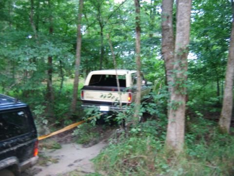 1992 Ford Mustang - A tan Ford Bronco is stuck in a muddy forest path, being pulled by a black SUV.