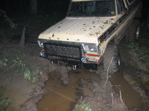 1992 Ford Mustang - A tan Ford Bronco is stuck in a muddy rut, its front tires submerged in water and mud.