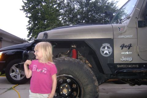 2004 Jeep Wrangler - A young girl stands beside a Jeep Wrangler, which has "SPORT" and "4x4" badging visible.