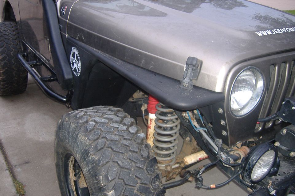 Close-up of a Jeep Wrangler's front tire, fender, and grille. Has a sticker that says WWW.JEEPFORUM.COM
