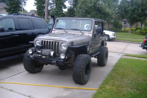 2004 Jeep Wrangler - A lifted 2004 Jeep Wrangler with off-road tires and a front-mounted winch is parked on a concrete driveway.