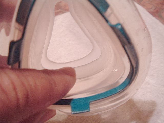 Hand holding a clear and teal silicone mask cushion