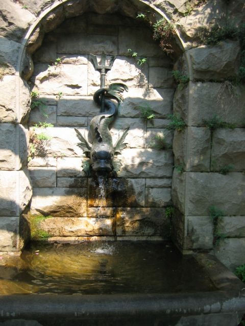 1985 Ford Crown Victoria LTD - A stone fountain a dragon-like sculpture with water spouting from its mouth into a basin below.