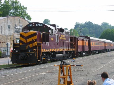 1985 Ford Crown Victoria LTD - A train with locomotive 1755 and passenger cars sits on railroad tracks near a building.
