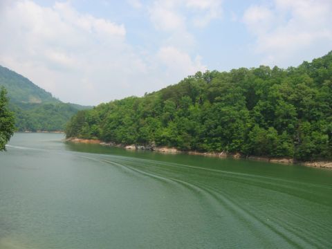 1985 Ford Crown Victoria LTD - A boat leaves a wake on a calm lake surrounded by lush green trees and hills.