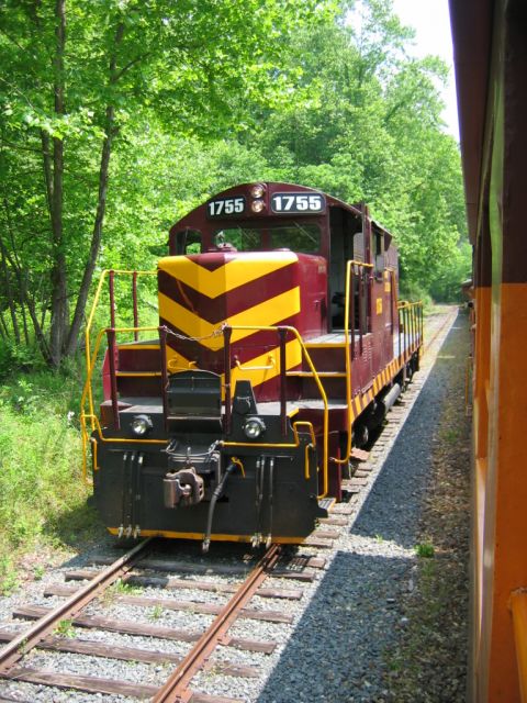 1985 Ford Crown Victoria LTD - A maroon and yellow locomotive, marked with the number 1755, sits on a railway track beside another train.