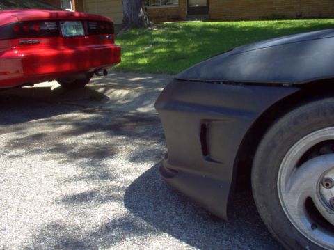 1994 Ford Probe - Two cars are parked on a street, one is a red 1994 Ford Probe seen from the rear, and the other is a black car's front corner.