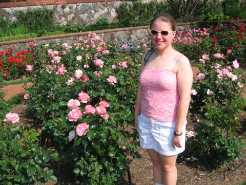1985 Ford Crown Victoria LTD - Woman posing in a garden filled with pink and red roses, with a stone wall in the background.