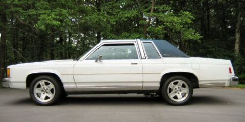 1985 Ford LTD Crown Victoria - Side view of a white sedan with a blue vinyl roof and chrome accents, parked outdoors.