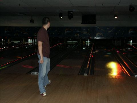 2001 Mercury Grand Marquis - A man stands on the wooden floor of a bowling alley, looking towards the lanes and pins.