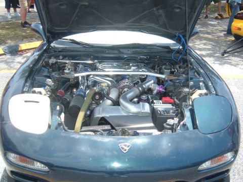 1989 Ford Probe - A dark teal Mazda RX-7 is displayed with its hood open, revealing a custom rotary engine setup.