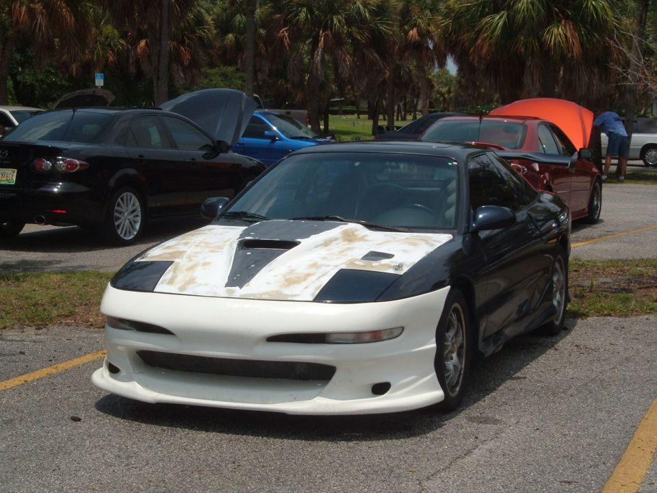 Front view of a dark blue and white sports coupe with a modified hood and bumper, parked outdoors with other cars