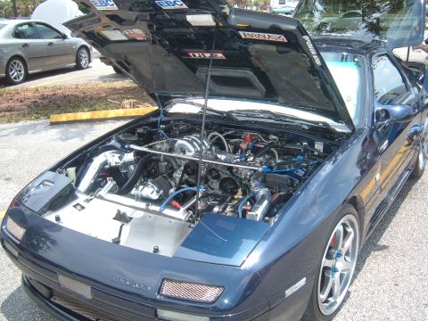 1989 Ford Probe - A dark blue Mazda RX-7 is displayed with its hood open, revealing a modified engine bay.