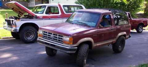 1979 Ford F-250 - Two Ford trucks, a Bronco II and an F-Series, are parked on a street with one's hood open.
