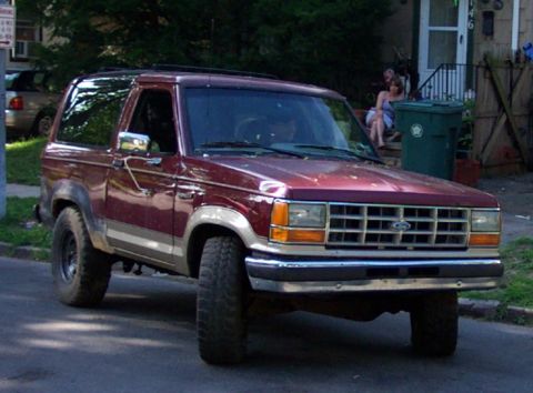 1979 Ford F-250 - Maroon Ford Bronco II drives down a residential street, showing its distinctive grille and body style.