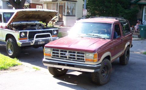 1979 Ford F-250 - A red Ford Bronco II is parked on a street, with another truck in the background. The Bronco II appears to be a 1989 model.