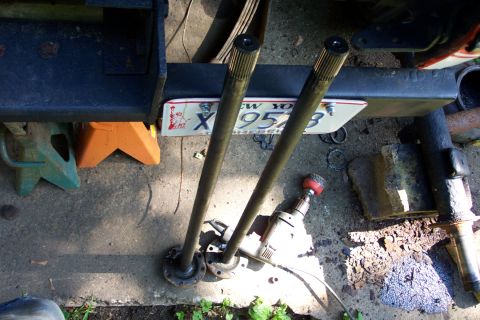 1978 Ford Bronco - Axle shafts and a New York license plate are visible on the ground, with a drill nearby.