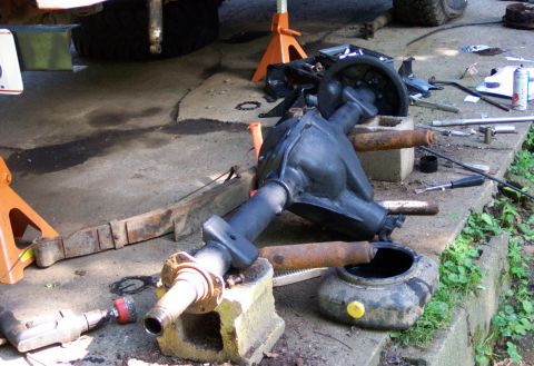 1978 Ford Bronco - A disassembled rear axle assembly lies on the ground with tools and a drain pan nearby.