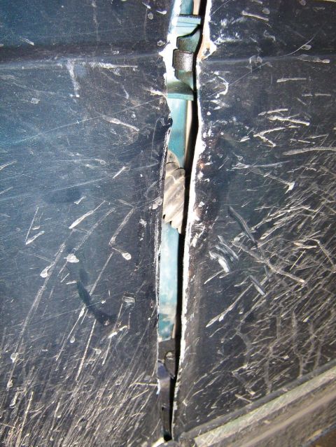 1995 Ford Bronco - The door gap of a dark blue vehicle reveals significant damage and numerous scratches across its surface.