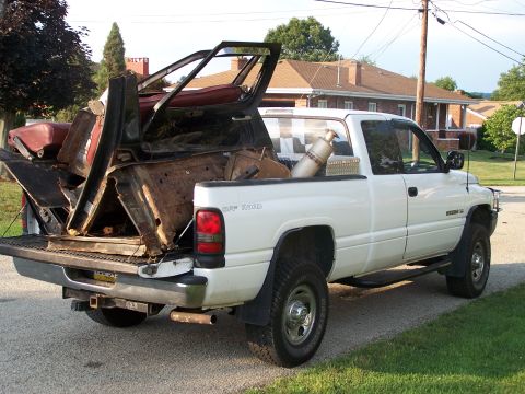 1986 Ford Bronco - White Dodge Ram pickup truck hauling a load of car parts and a propane tank.
