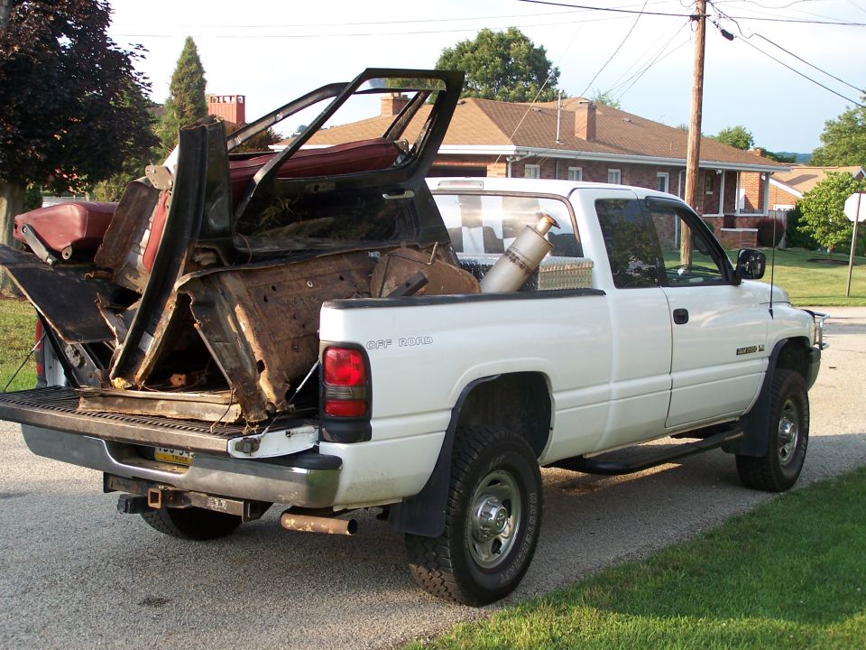 White Dodge Ram 1500 pickup loaded with scrap body panels and a roll bar in the bed