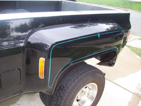 2005 Dodge 1500 - Close-up view of the rear fender of a black pickup truck, distinctive blue pinstripes and an amber marker light.