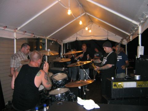 1986 Ford Mustang - A band plays music under a tent, with a drummer in the foreground and other band members visible.
