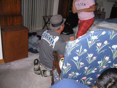 1986 Ford Mustang - A man wearing a fedora and a t-shirt with a graphic print kneels on the floor in a room.
