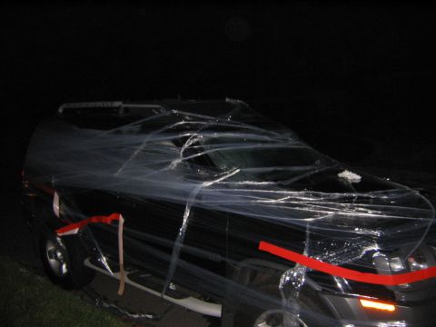 1986 Ford Mustang - A black SUV is completely wrapped in clear plastic and secured with red tape.