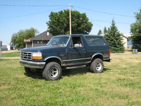 1995 Ford Bronco - This dark blue 1995 Ford Bronco is parked on a grassy area with houses and trees in the background.