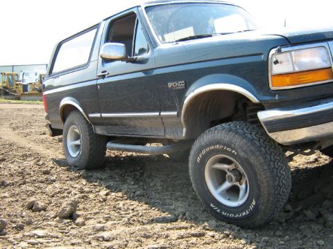 1995 Ford Bronco - A Ford Bronco is parked on a dirt lot, with construction equipment visible in the distance.